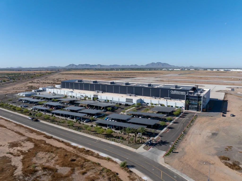 Aerial view of a large Gulfstream facility with solar panel carports, desert landscape, and distant mountains under a clear sky.