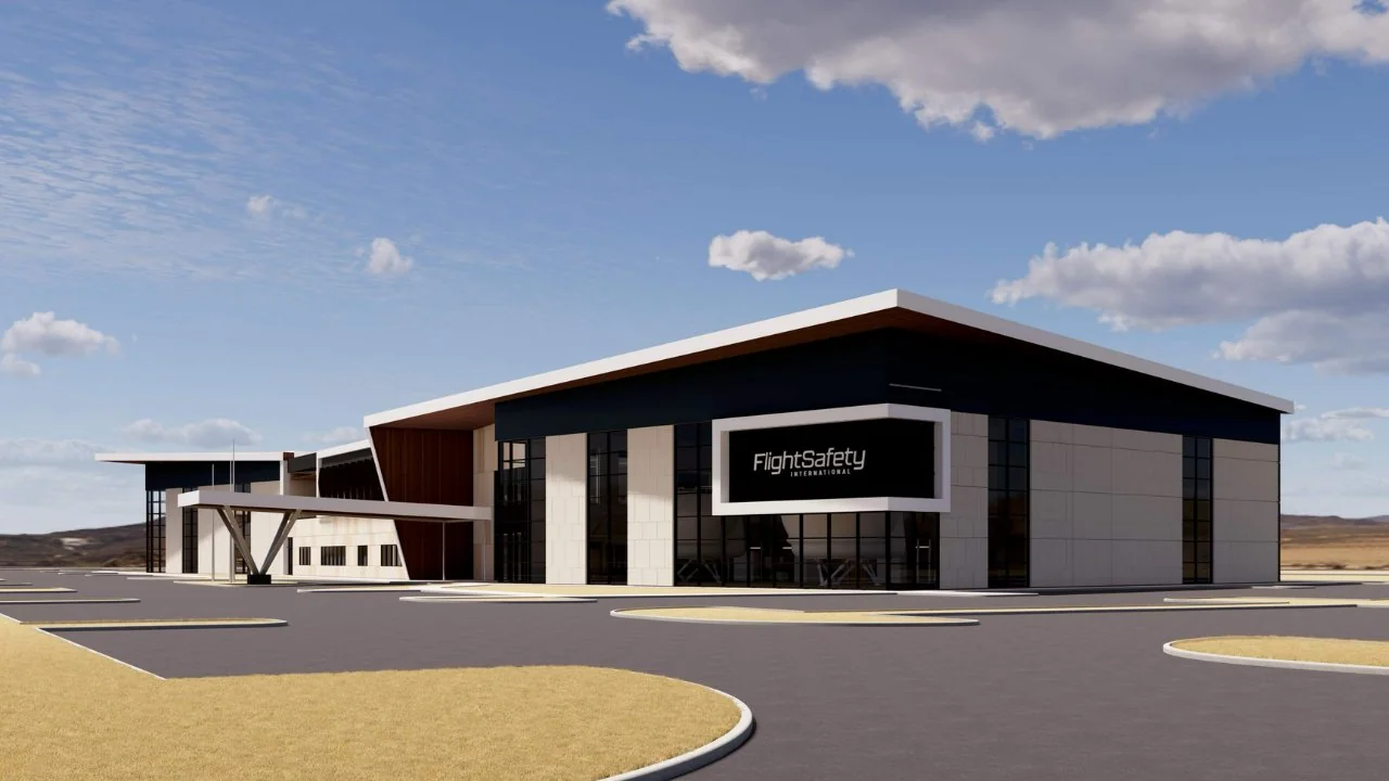 A modern FlightSafety International building with a flat roof, large windows, and a covered entrance, surrounded by a paved lot and dry landscape.