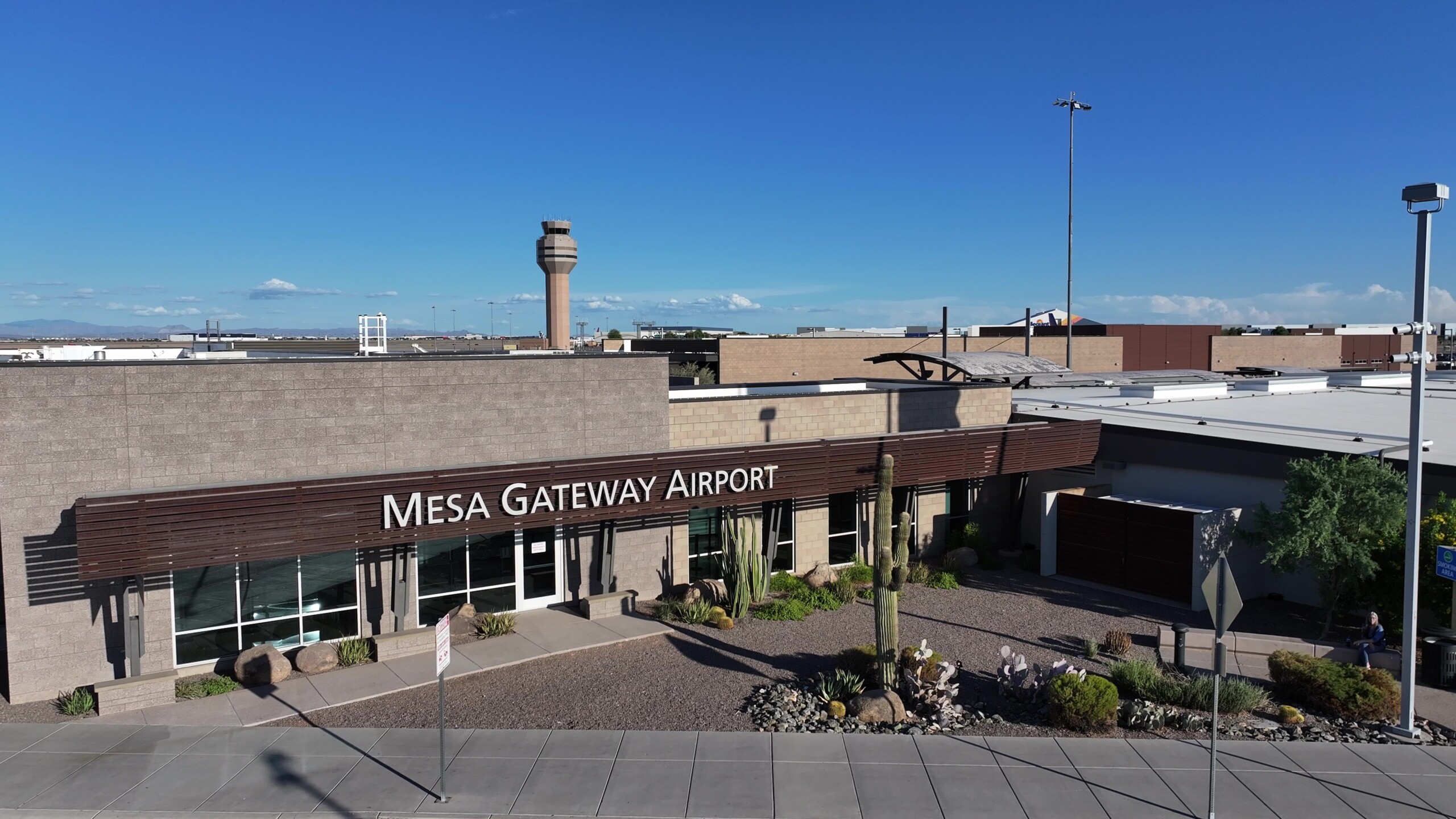 Aerial view of Mesa Gateway Airport building with desert landscaping, a control tower in the background, and clear blue skies.