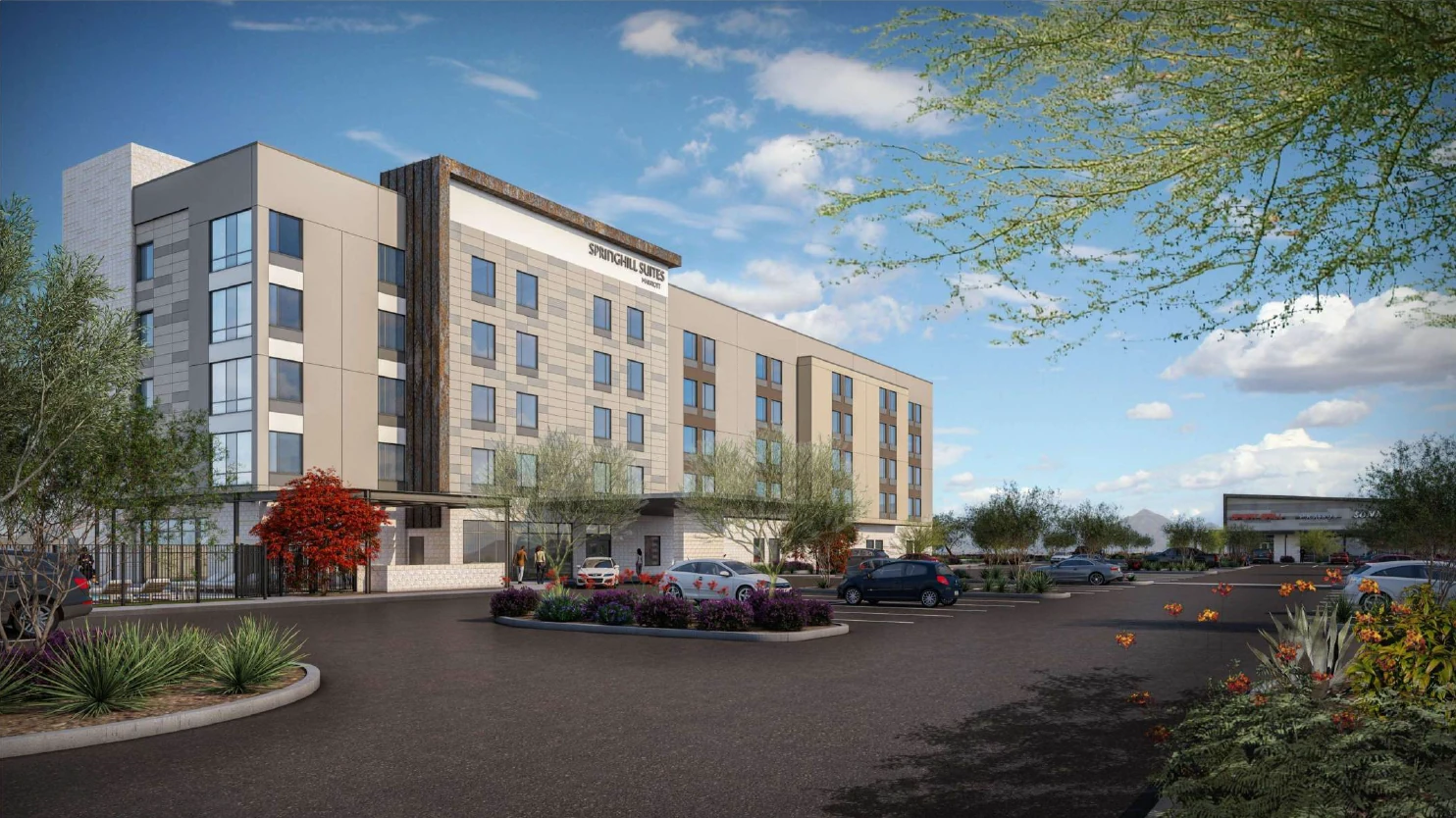 Exterior view of a modern SpringHill Suites by Marriott hotel with a large parking lot and desert landscaping under a blue sky.